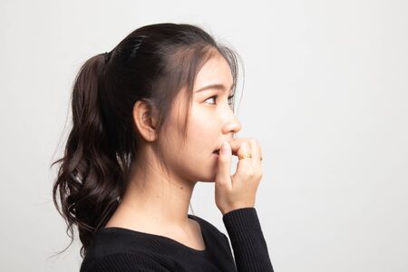 Unsure hesitant nervous young asian  woman biting her fingernails on white backgroundの写真素材
