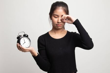 Sleepy young Asian woman with a clock in the morning on white backgroundの写真素材