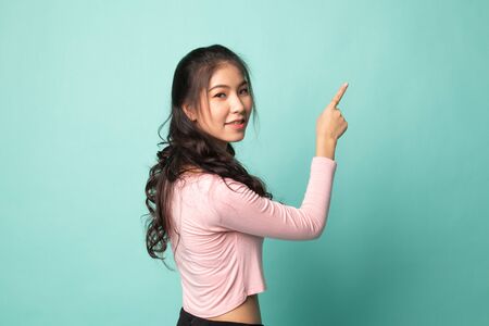 Back of Asian woman touching the screen with her finger on cyan backgroundの写真素材