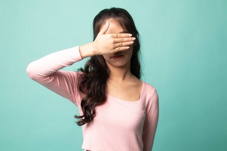 Young Asian woman close her eyes with hand on cyan backgroundの写真素材