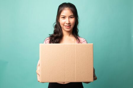 Delivery, relocation and unpacking.  young asian woman holding cardboard box on cyan backgroundの写真素材