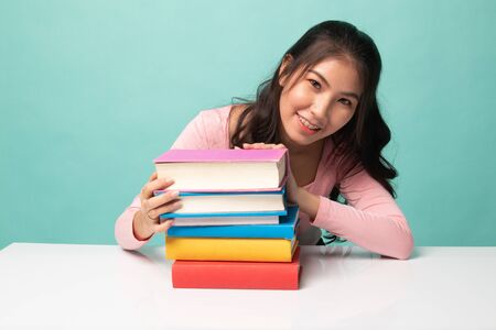 Happy young Asian woman read a book with books on table on cyan backgroundの写真素材