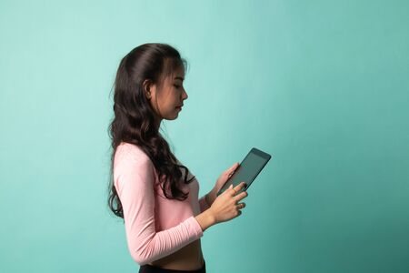 Young Asian woman with a computer tablet on cyan backgroundの写真素材