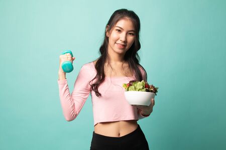 Healthy Asian woman with dumbbells and salad on cyan backgroundの写真素材