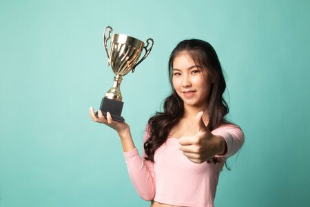 Successful young asian woman holding a trophy show thumb up on cyan backgroundの写真素材