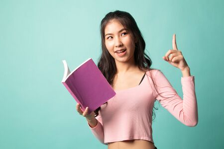 Young Asian woman with a book have an idea on cyan backgroundの写真素材