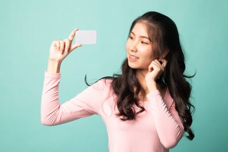 Happy young Asian woman with a blank card on cyan backgroundの写真素材