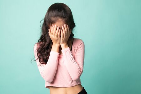 Sad young Asian woman cry with palm to face on cyan backgroundの写真素材