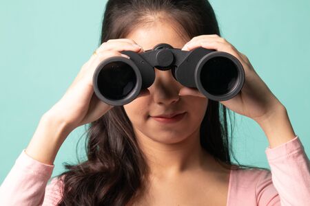Young Asian woman with binoculars on cyan backgroundの写真素材