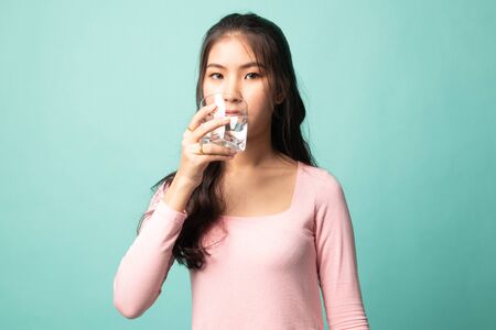 Young Asian woman with a glass of drinking water on cyan backgroundの写真素材