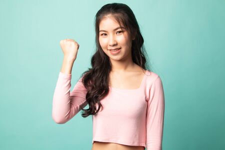 Successful  young Asian woman hold fist up on cyan backgroundの写真素材