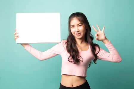 Young Asian woman show OK with  white blank sign on cyan backgroundの写真素材