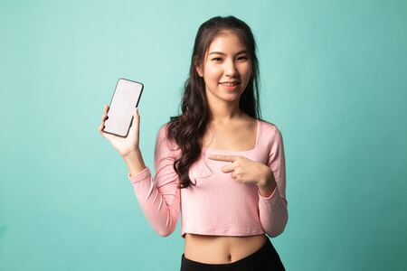 Young Asian woman point to mobile phone on cyan backgroundの写真素材