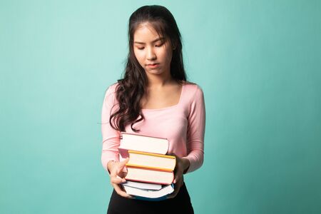 Unhappy young Asian woman studying  with may books on cyan backgroundの写真素材