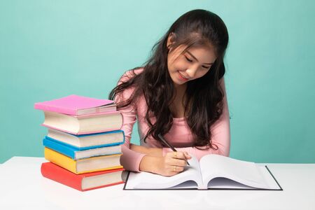 Young Asian woman read a book with books on table on cyan backgroundの写真素材
