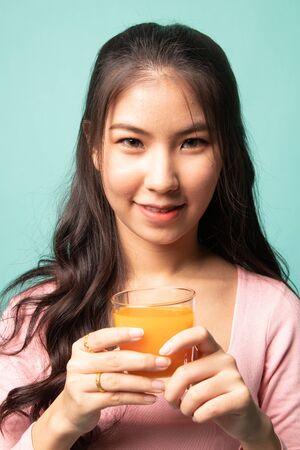 Young Asian woman drink orange juice on cyan backgroundの写真素材