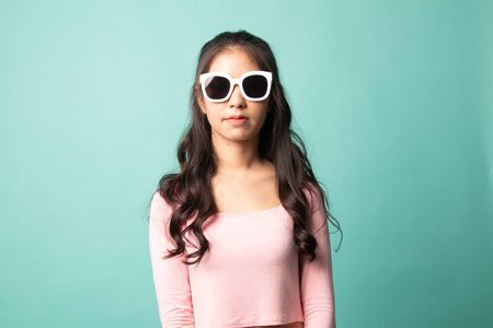 Portrait of a beautiful young asian girl in sunglasses on cyan backgroundの写真素材