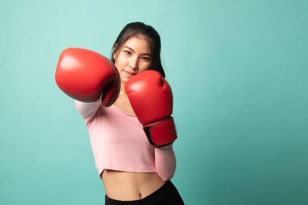 Young Asian woman with red boxing gloves on cyan backgroundの写真素材