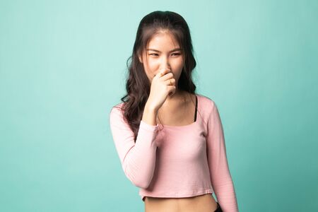 Young Asian woman  holding her nose because of a bad smell on cyan backgroundの写真素材