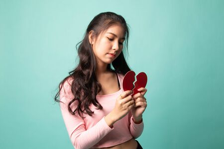 Beautiful young Asian woman with broken heart on cyan backgroundの写真素材