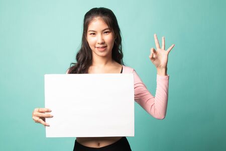 Young Asian woman show OK with white blank sign on cyan backgroundの写真素材