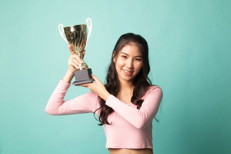 Successful young asian woman holding a trophy on cyan backgroundの写真素材