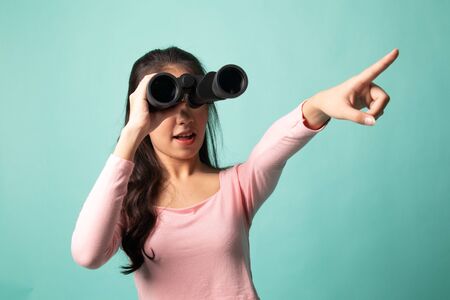 Young Asian woman  point and look with binoculars on cyan backgroundの写真素材