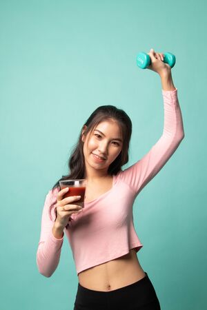 Young healthy Asian woman with dumbbell and  tomato juice on cyan backgroundの写真素材