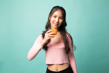 Young Asian woman drink orange juice on cyan backgroundの写真素材
