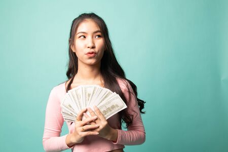 Portrait of  young asian woman  showing bunch of money banknotes on cyan backgroundの写真素材