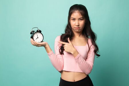 Angry young Asian woman point to a clock on cyan backgroundの写真素材