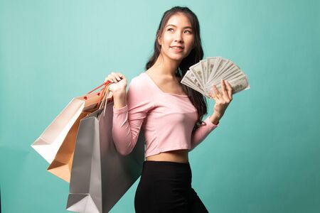 Portrait of  young asian woman  showing bunch of money banknotes on cyan backgroundの写真素材
