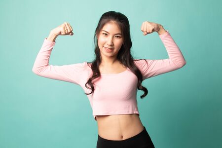 Beautiful young Asian woman flex bicep on cyan backgroundの写真素材