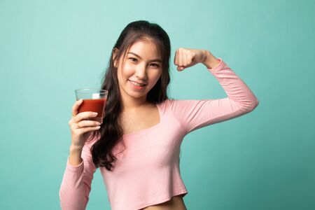 Strong healthy Asian woman with tomato juice on cyan backgroundの写真素材