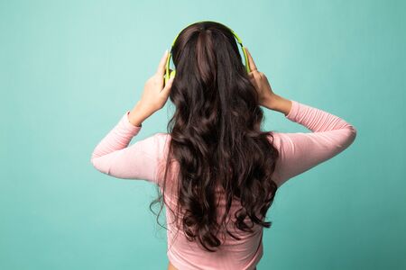 Pretty asian girl listening music with her headphones on cyan backgroundの写真素材