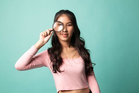 Young Asian woman with a magnifying glass on cyan backgroundの写真素材