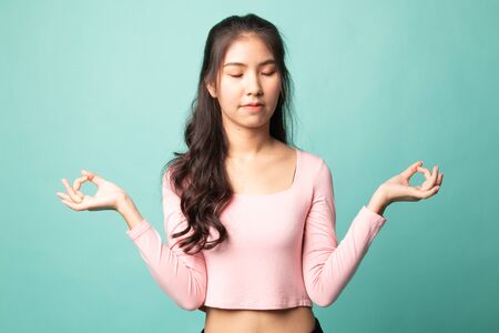 Concentrated relaxed  asian  female  closed eyes, having relaxation while meditating, trying to find balance and harmony Yoga and meditation concept on cyan backgroundの写真素材