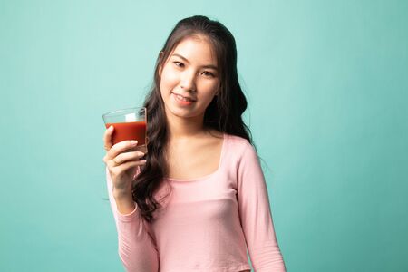 Young Asian woman drink tomato juice on cyan backgroundの写真素材