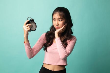 Young Asian woman is stressed with a clock on cyan backgroundの写真素材