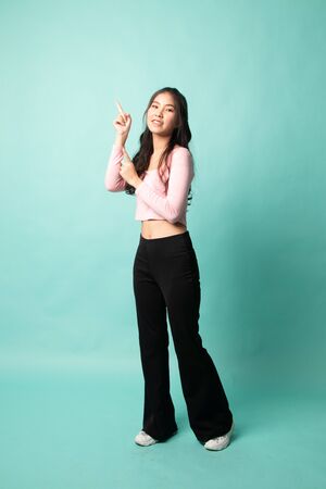 Full body of beautiful young asian woman pointing up on cyan backgroundの写真素材