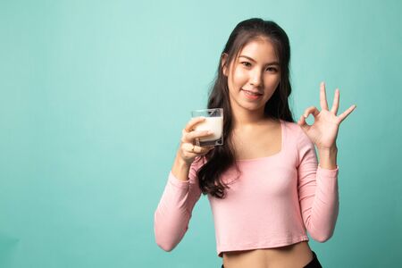 Healthy Asian woman drinking a glass of milk show OK sign on cyan backgroundの写真素材
