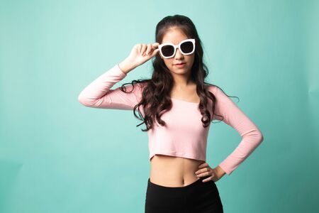 Portrait of a beautiful young asian girl in sunglasses on cyan backgroundの写真素材
