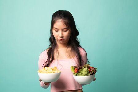 Young Asian woman with potato chips and salad on cyan backgroundの写真素材