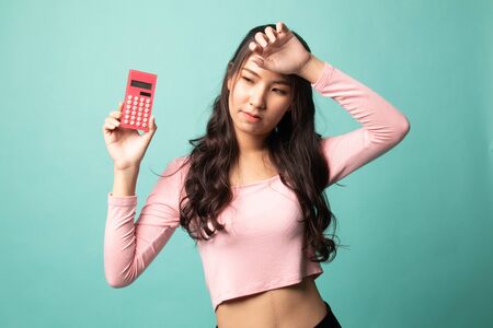 Asian woman got  headache with calculator on cyan backgroundの写真素材