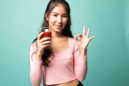 Young Asian woman show OK with tomato juice on cyan backgroundの写真素材