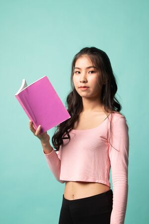 Young Asian woman read a book on cyan backgroundの写真素材