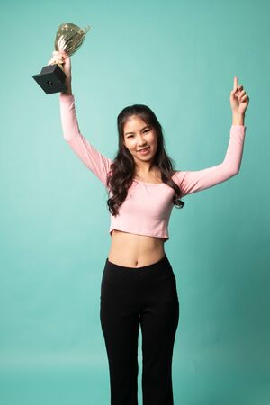 Successful number one winner young asian woman holding a trophy on cyan backgroundの写真素材