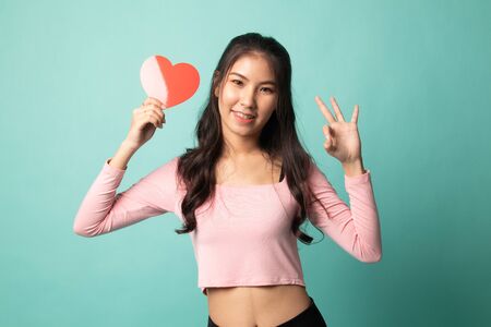 Asian woman show OK with red heart on cyan backgroundの写真素材