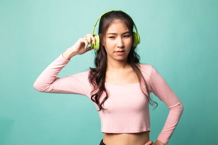 Too loud.  portrait of  young asian woman  holding  headphones and making unhappy face on cyan backgroundの写真素材