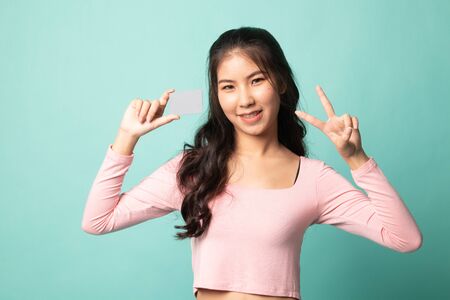 Young Asian woman show Victory with a blank card on cyan backgroundの写真素材